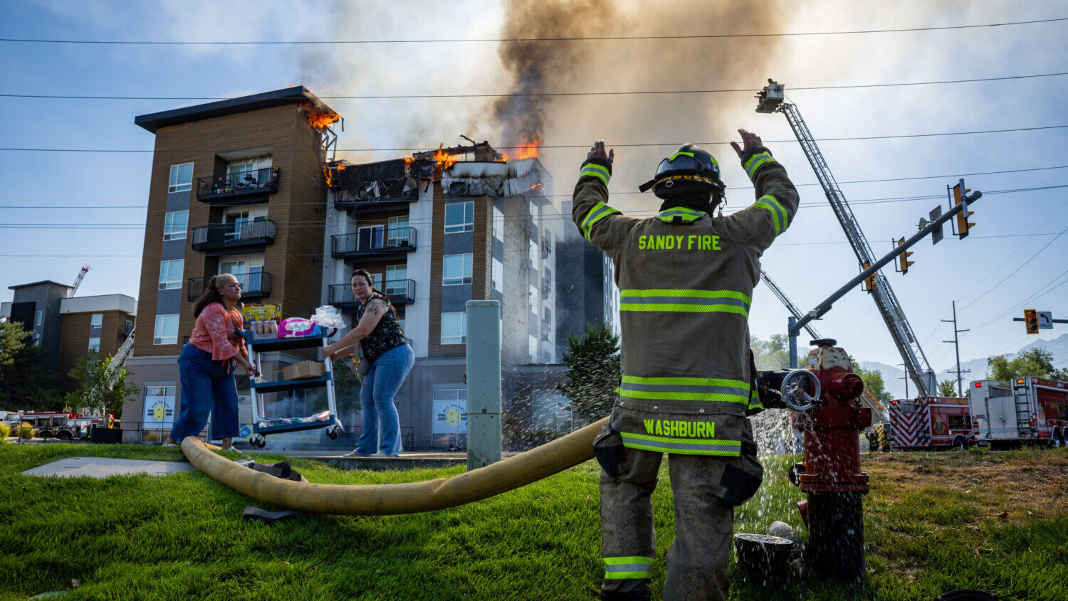 A member of the Sandy City Fire Department motions after connecting a hose to a fire hydrant as fellow firefighters respond to an apartment fire at 942 E. North Union Ave. near Hillcrest High School in Midvale on Friday, July 31, 2026. (Tess Crowley, Deseret News)